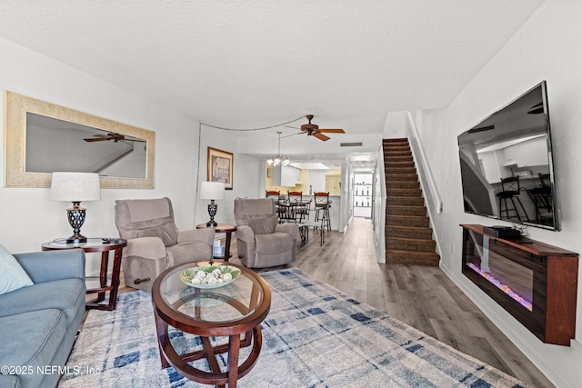 living area with a textured ceiling, stairway, wood finished floors, and ceiling fan with notable chandelier
