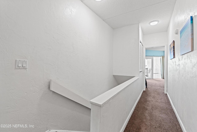 corridor with baseboards, a textured ceiling, carpet, and a textured wall