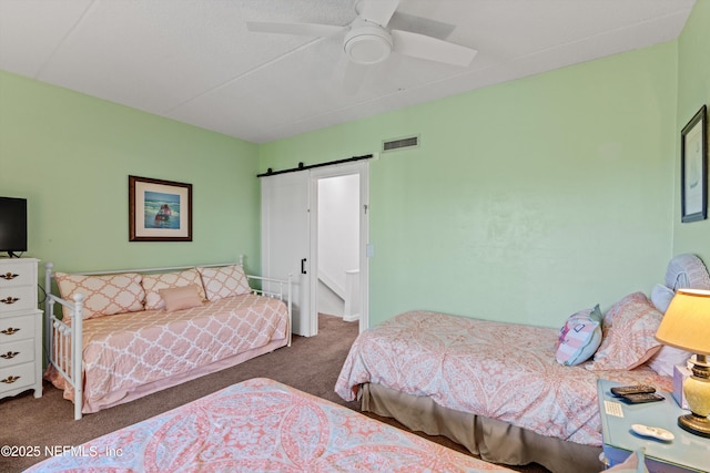 carpeted bedroom featuring a ceiling fan, visible vents, and a barn door