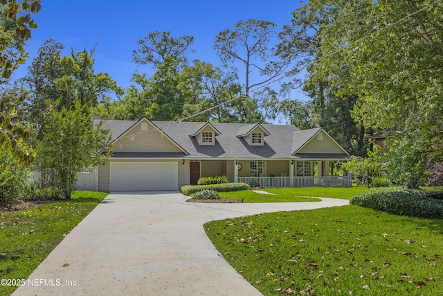 new england style home with roof with shingles, an attached garage, a front lawn, covered porch, and driveway