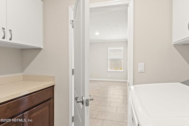 clothes washing area with crown molding, washing machine and dryer, light tile patterned flooring, baseboards, and cabinet space
