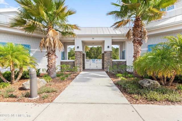 doorway to property with a gate, driveway, metal roof, and stone siding