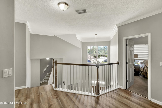 hall featuring crown molding, visible vents, wood finished floors, baseboards, and a notable chandelier