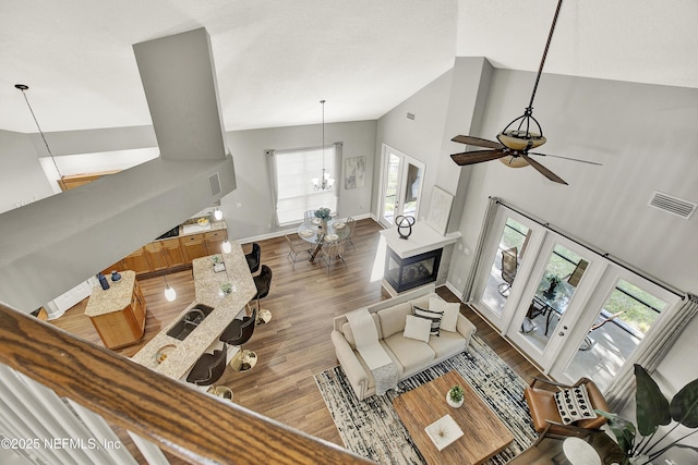 living area with visible vents, ceiling fan with notable chandelier, a wealth of natural light, and high vaulted ceiling