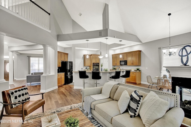 living area with decorative columns, high vaulted ceiling, baseboards, a notable chandelier, and light wood-style flooring