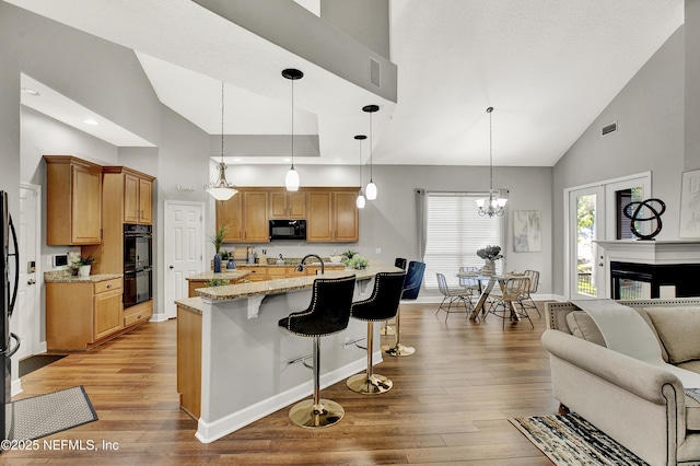 kitchen with a breakfast bar area, light stone countertops, high vaulted ceiling, baseboards, and black appliances