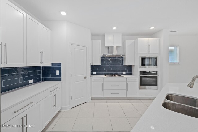 kitchen with stainless steel appliances, a sink, wall chimney range hood, light countertops, and white cabinets