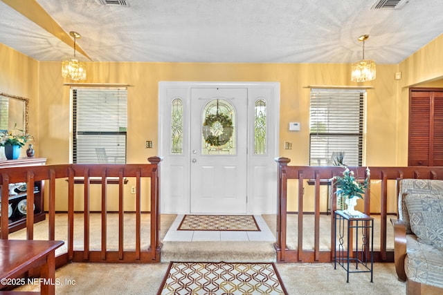 carpeted entrance foyer featuring visible vents, a textured ceiling, and a notable chandelier