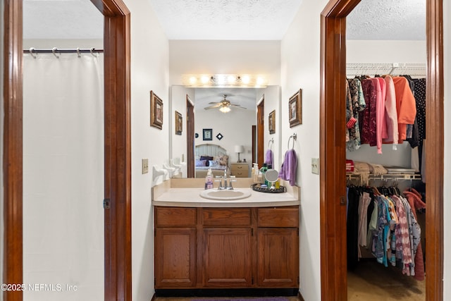 full bath with vanity, ceiling fan, a textured ceiling, a spacious closet, and ensuite bath