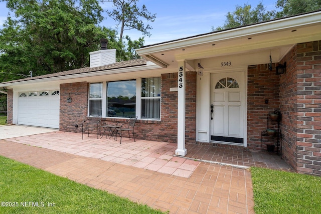 entrance to property with brick siding, an attached garage, driveway, and a chimney