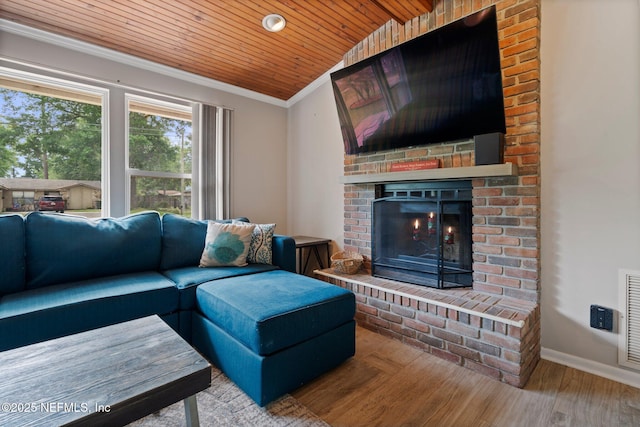 living area with wood ceiling, crown molding, a brick fireplace, wood finished floors, and baseboards