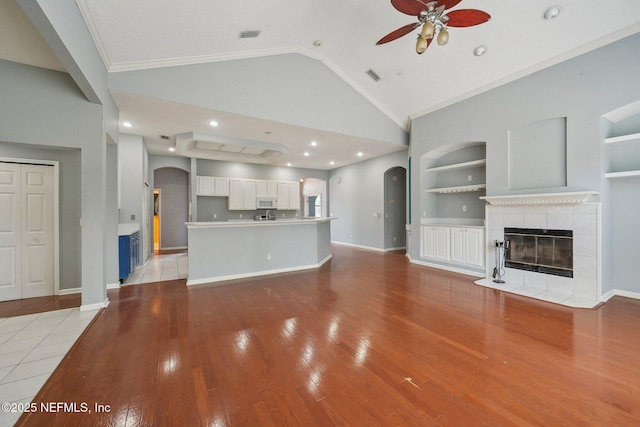 unfurnished living room featuring arched walkways, a ceiling fan, light wood-type flooring, lofted ceiling, and a tile fireplace