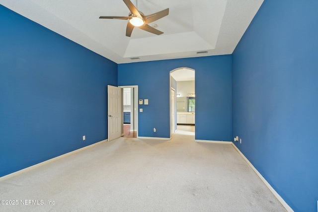 unfurnished bedroom with a raised ceiling, carpet floors, arched walkways, baseboards, and visible vents