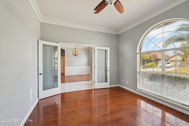 empty room with crown molding, french doors, ceiling fan with notable chandelier, and wood finished floors
