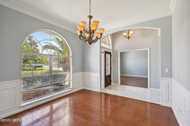 foyer with crown molding, wainscoting, wood finished floors, and a notable chandelier