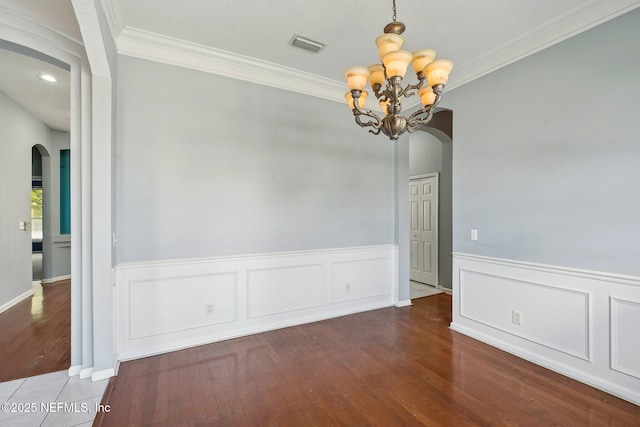 unfurnished dining area featuring visible vents, arched walkways, wood finished floors, a notable chandelier, and ornamental molding