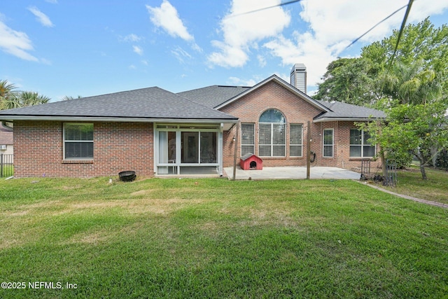 rear view of house featuring a chimney, roof with shingles, brick siding, a yard, and a patio