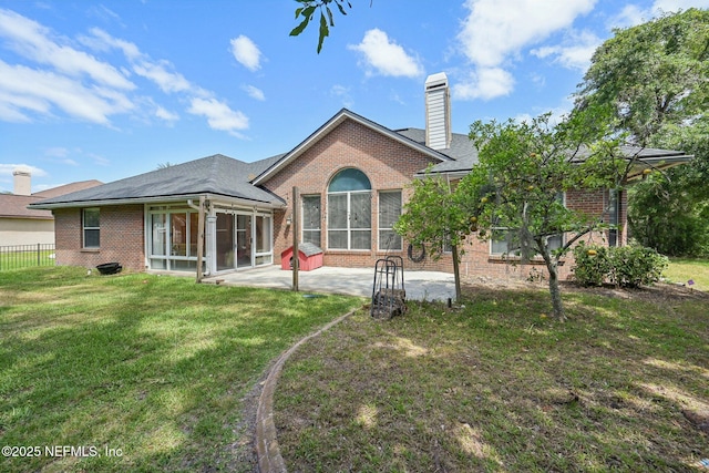 back of property featuring a chimney, brick siding, a sunroom, a patio area, and a lawn