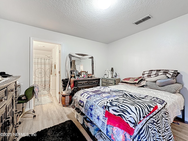 bedroom featuring visible vents, connected bathroom, a textured ceiling, and wood finished floors