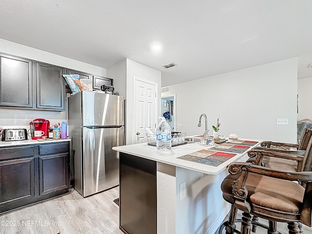 kitchen featuring visible vents, freestanding refrigerator, a breakfast bar, light wood-type flooring, and light countertops