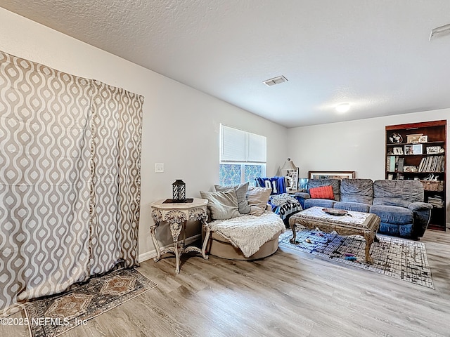 living room featuring a textured ceiling, visible vents, and wood finished floors