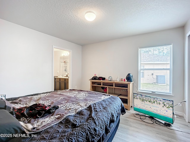 bedroom with connected bathroom, a textured ceiling, and light wood-style flooring