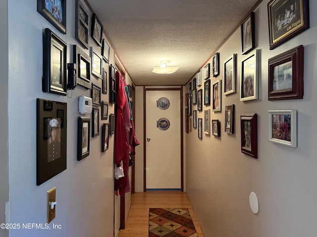 hallway with a textured ceiling, baseboards, and light wood finished floors