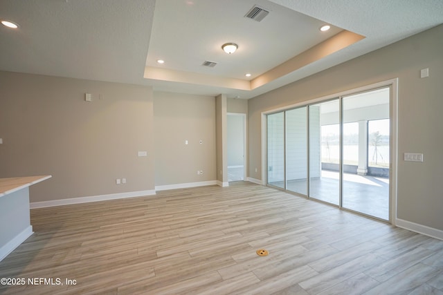 unfurnished living room featuring light wood-type flooring, recessed lighting, baseboards, and a tray ceiling