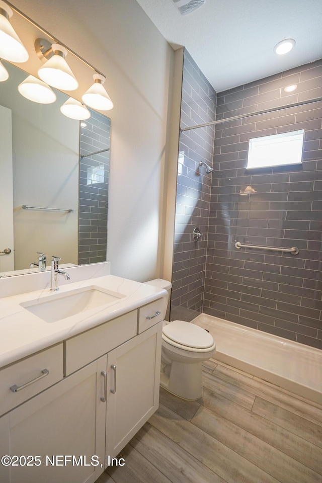 full bath with vanity, a tile shower, toilet, and wood finished floors