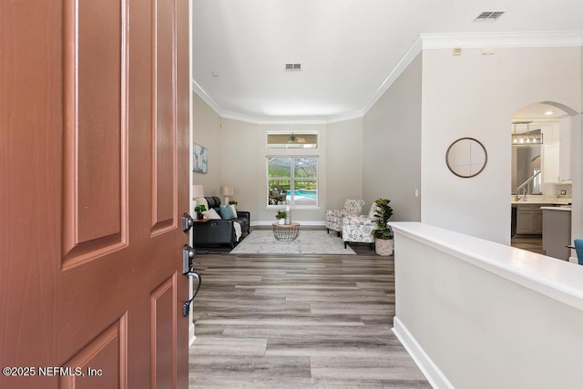 foyer featuring crown molding, baseboards, arched walkways, and light wood-style floors