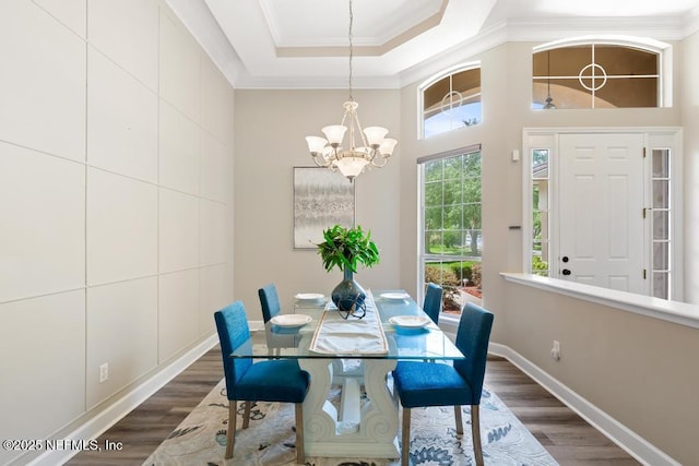 dining room with dark wood-type flooring, ornamental molding, a chandelier, baseboards, and a raised ceiling