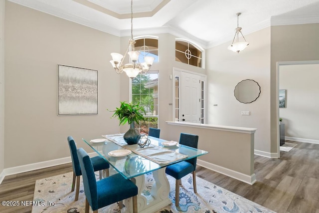 dining area with ornamental molding, a chandelier, wood finished floors, baseboards, and a high ceiling