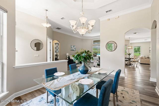 dining space with arched walkways, a chandelier, wood finished floors, ornamental molding, and baseboards