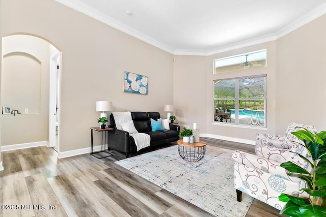 living room featuring wood finished floors, crown molding, arched walkways, and baseboards