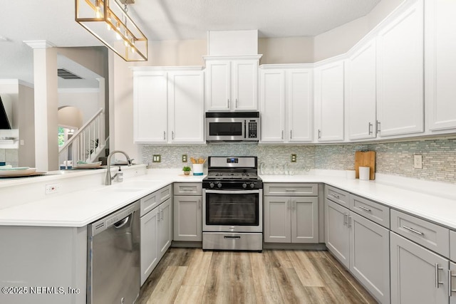 kitchen featuring appliances with stainless steel finishes, a sink, gray cabinets, a peninsula, and tasteful backsplash