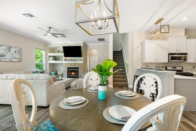 dining area featuring light wood-type flooring, stairway, crown molding, ceiling fan, and a fireplace