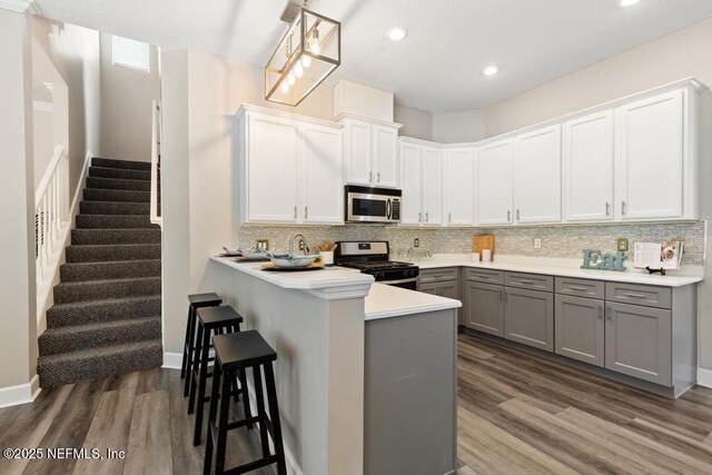 kitchen with appliances with stainless steel finishes, gray cabinets, wood finished floors, a kitchen breakfast bar, and backsplash