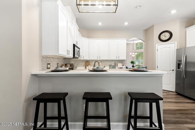 kitchen featuring stainless steel appliances, a peninsula, tasteful backsplash, white cabinetry, and a breakfast bar
