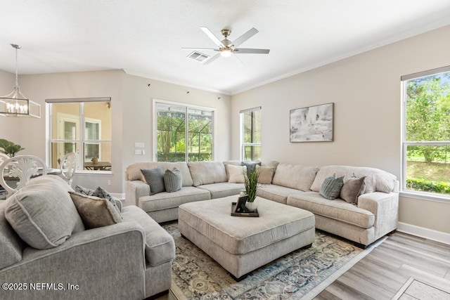 living room featuring light wood-type flooring, a chandelier, baseboards, ornamental molding, and a ceiling fan