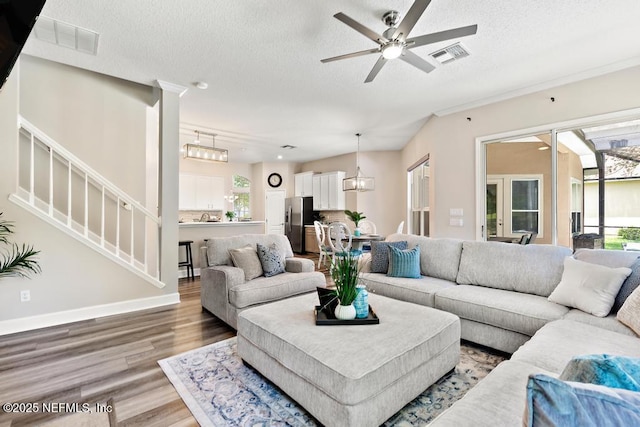 living room featuring wood finished floors, a textured ceiling, plenty of natural light, ceiling fan, and stairs