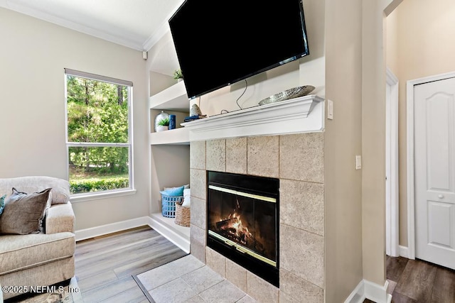 living area with a fireplace, crown molding, wood finished floors, plenty of natural light, and baseboards