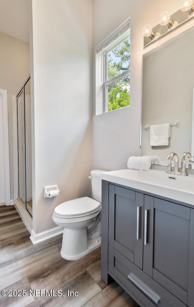 bathroom featuring toilet, a shower stall, wood finished floors, vanity, and baseboards