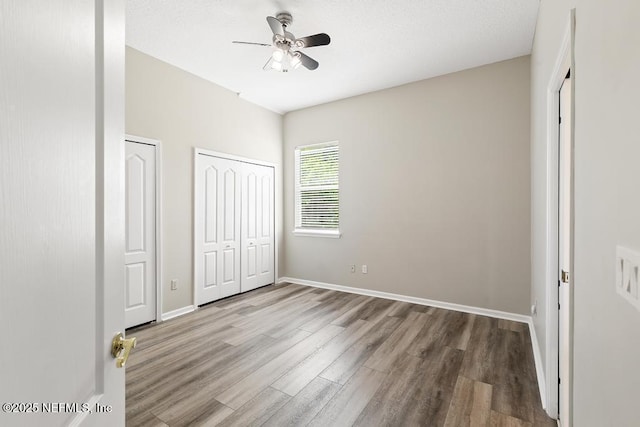 unfurnished bedroom with wood finished floors, multiple closets, baseboards, and a ceiling fan