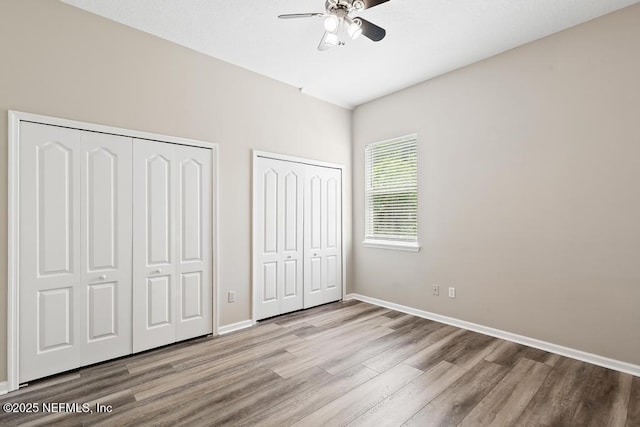 unfurnished bedroom featuring two closets, wood finished floors, baseboards, and a ceiling fan