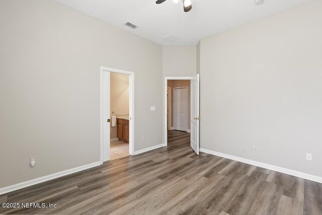 unfurnished bedroom with wood finished floors, baseboards, ensuite bath, and ceiling fan