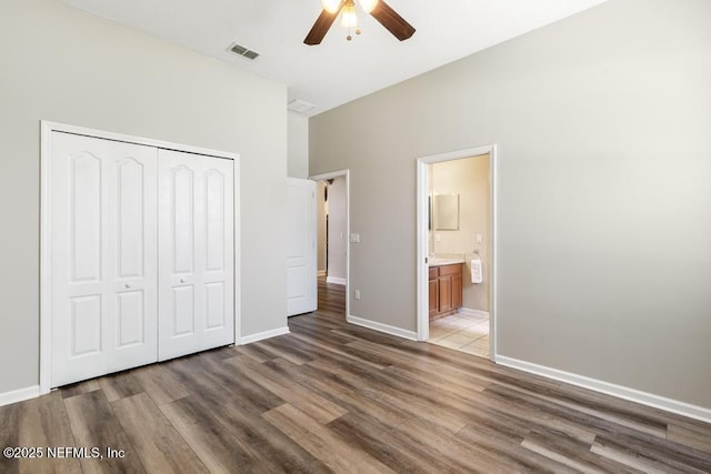 unfurnished bedroom with wood finished floors, a closet, baseboards, ceiling fan, and connected bathroom