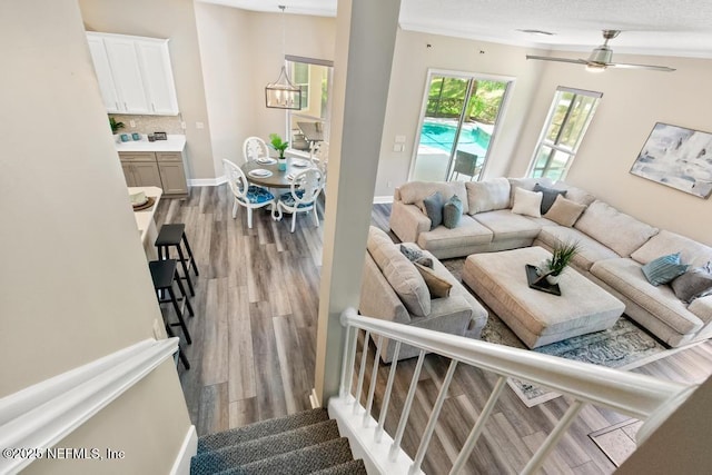 living room with wood finished floors, stairs, a ceiling fan, baseboards, and a chandelier