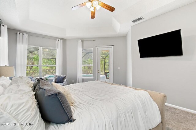 carpeted bedroom with a raised ceiling, access to exterior, and a ceiling fan