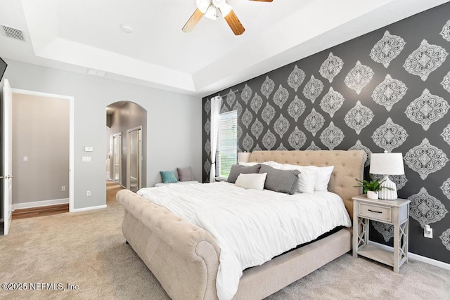 carpeted bedroom with arched walkways, a tray ceiling, baseboards, and a ceiling fan