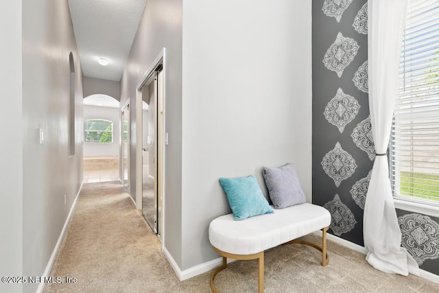 hallway featuring carpet, baseboards, and arched walkways